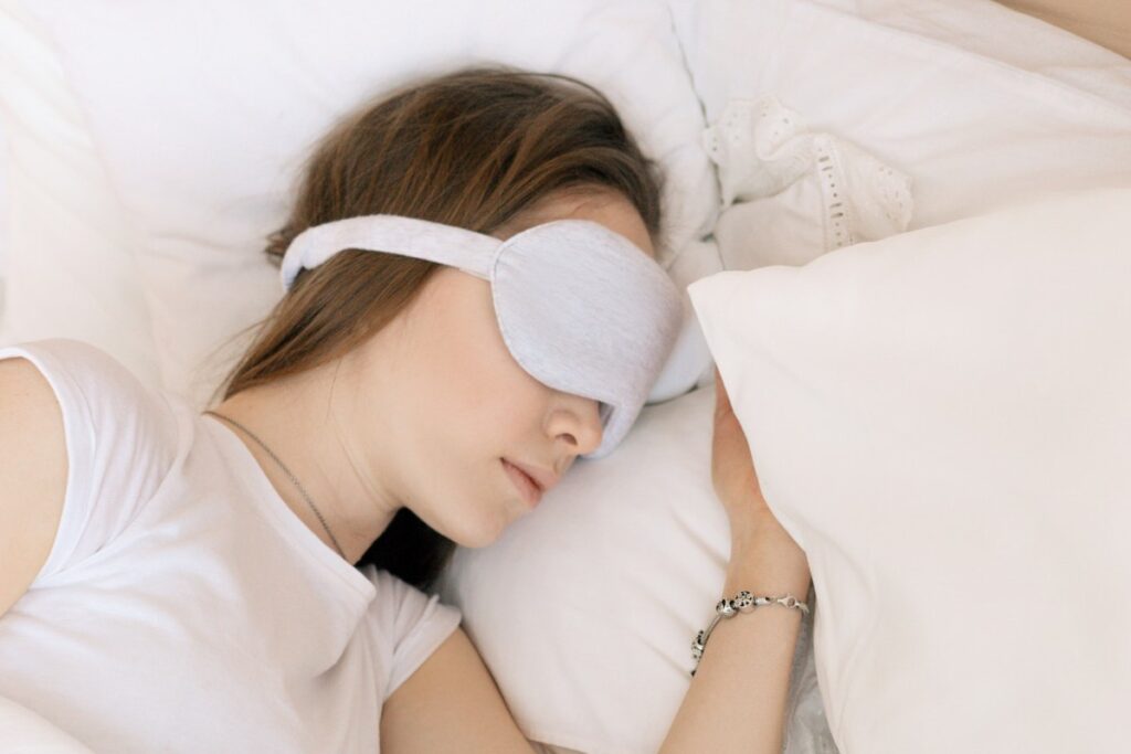 Women sleeping in a bed with an eye mask on.