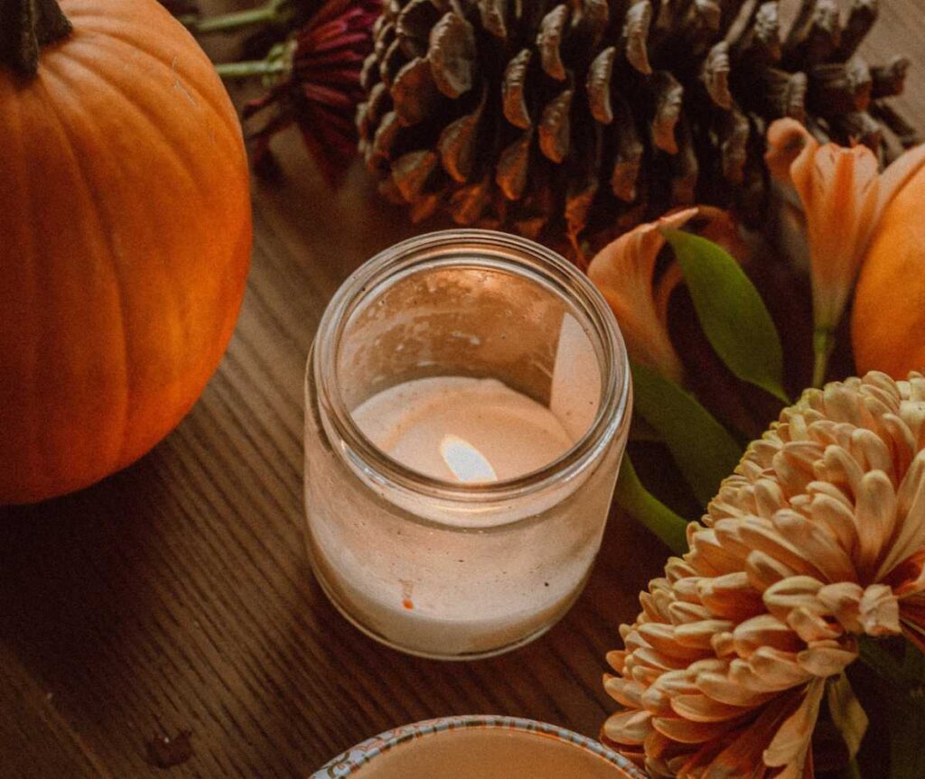 Scented mason jar candle on table with pumpkins, pinecones and fall florals.