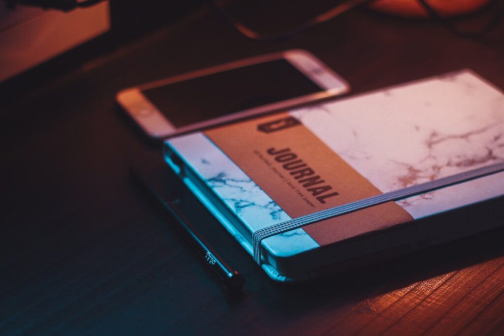 A journal notebook sitting on a table next to a pen and a cell phone. 